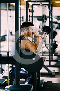 Attractive Young Man Doing Heavy Weight Exercise For Biceps On Machine In A Gym