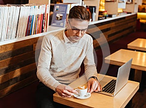 Attractive young man drinking coffee and using laptop.