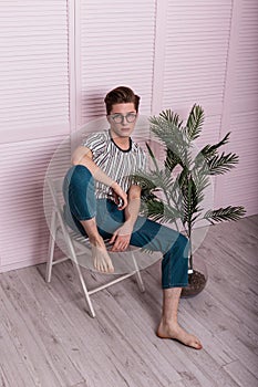 Attractive young man with a fashionable hairstyle in stylish youth summer clothes in vintage glasses is resting on a chair next to