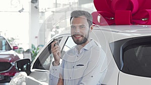 Attractive young man holding car keys to his new automobile at dealership