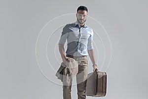 Attractive young man with jacket and suitcase posing in a fashion way