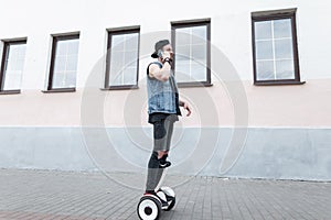 Attractive young man in a jeans vest in ripped jeans in a cap in a t-shirt in sneakers rides on a white gyroscope