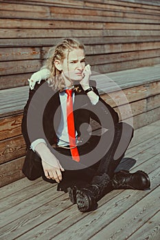 Attractive young man with long blonde hair in a black suit and red tie, rats running around his body. His face expresses