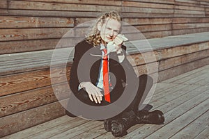 Attractive young man with long blonde hair in a black suit and red tie, rats running around his body. His face expresses