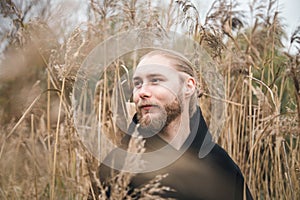 An attractive young man looks into the distance among the tall reeds.