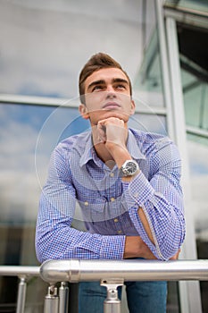 Attractive young man on the office building background. A serious corporate worker with a watch. Office work concept.