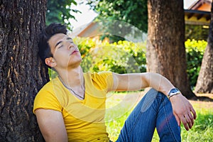 Attractive young man in park resting against tree