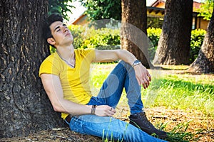 Attractive young man in park resting against tree