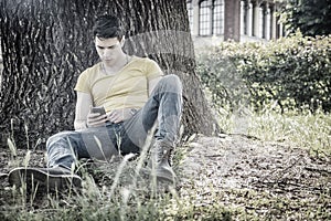 Attractive young man in park resting against tree