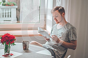 Attractive young man is reading a book at home. Thoughtful guy reading important book