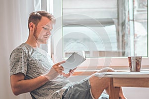 Attractive young man is reading a book at home. Thoughtful guy reading important book