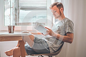 Attractive young man is reading a book at home. Thoughtful guy reading important book