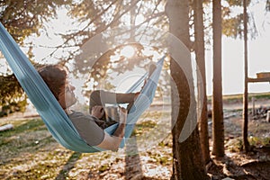 Attractive young man resting in hammock with coffee, tea in hammock in forest. Rear.