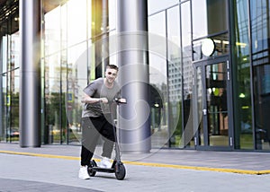 Attractive young man riding a kick scooter at cityscape background