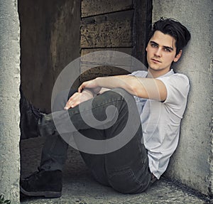 Attractive young man sitting on old door's threshold