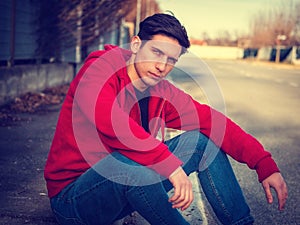 Attractive young man sitting on street curb