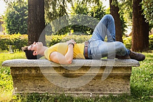 Attractive young man sleeping on stone bench