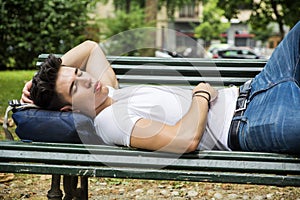 Attractive young man sleeping on wooden bench