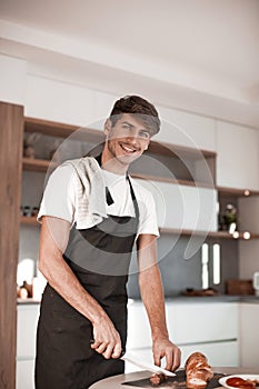 Attractive young man slicing sausage for sandwiches