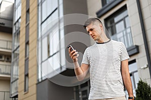 Attractive young man is standing on the street with a phone in his hands. Business handsome guy with a stylish hairstyle