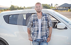 An attractive young man stands near a car.