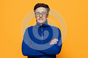 an attractive young man stands on an orange background in a blue zip-up jacket and black eyeglasses and looks into the