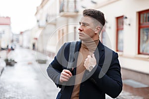 Attractive young man with a stylish hairstyle in a fashionable warm coat in a vintage knitted sweater with a fashionable black