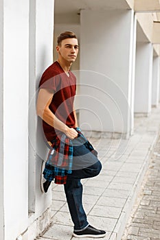 Attractive young man in stylish sneakers in a trendy T-shirt in a checkered colorful fashionable shirt in blue jeans standing near