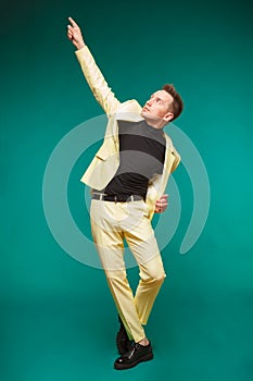 Attractive young man in suit dancing, having fun on mint background. Stylish outlook, successful businessman, happy