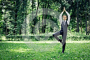 Attractive young man in a suit does yoga tree pose