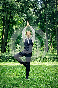 Attractive young man in a suit does yoga tree pose in a park