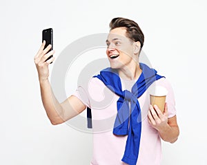 Attractive young man taking a selfie and holding takeaway coffee cup over white background