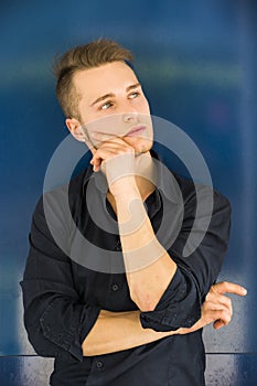 Attractive young man thinking, looking up with hand on his chin