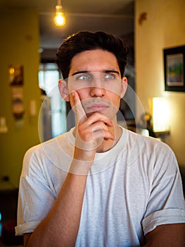 Attractive young man thinking, looking up with hand on his chin