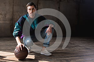 attractive young man in vintage windcheater with basketball ball sitting squats photo