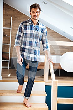 Attractive young man walking barefoot on stairs at home