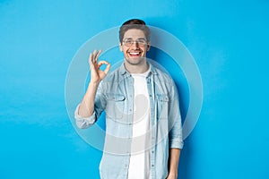 Attractive young man wearing glasses and casual clothes, showing ok good sign in approval, like something, standing