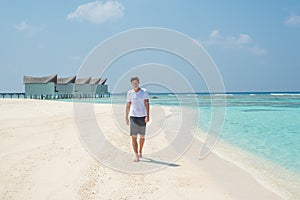 Attractive young man wearing t-shirt and shorts walking at tropical beach at island luxury resort