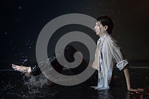 Attractive young man in white wet clothes in small pool under drops of the rain. Studio photo