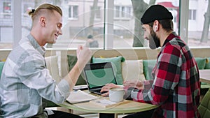 Attractive young men together discussing and doing a work project on the laptop in the coffee shop they using the