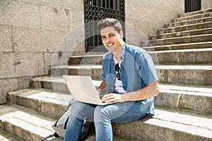 Attractive young modern man working with computer in the city on outside stairs