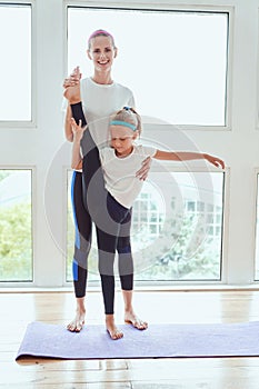 Attractive young mom with her little charming daughter are working out indoors. Doing yoga at home together. Fitness day