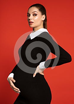 Attractive young pregnant woman in strict dress looking at camera