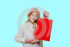 Attractive young red-haired girl with gift bags after shopping on a blue background looking towards the camera