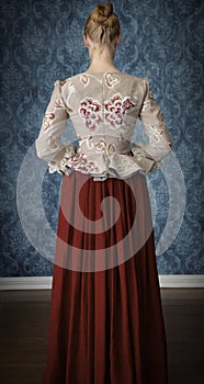 Red-haired 18th century woman standing in front of baroque wall paper