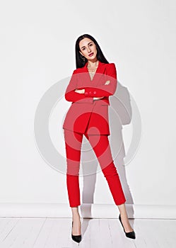Attractive young slim brunette woman in red business smart suit and high heels shooes standing and looking at camera