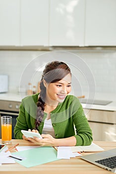 Attractive young smiling Woman paying bills online using laptop from home while sitting in the kitchen
