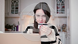 Attractive young smiling woman uses plastic credit card shopping online with laptop.