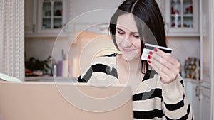 Attractive young smiling woman uses plastic credit card shopping online with laptop. slider to the right