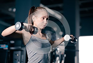 Attractive Young Sports Woman Lifting Dumbbells in the Gym. Fitness and Healthy Lifestyle.